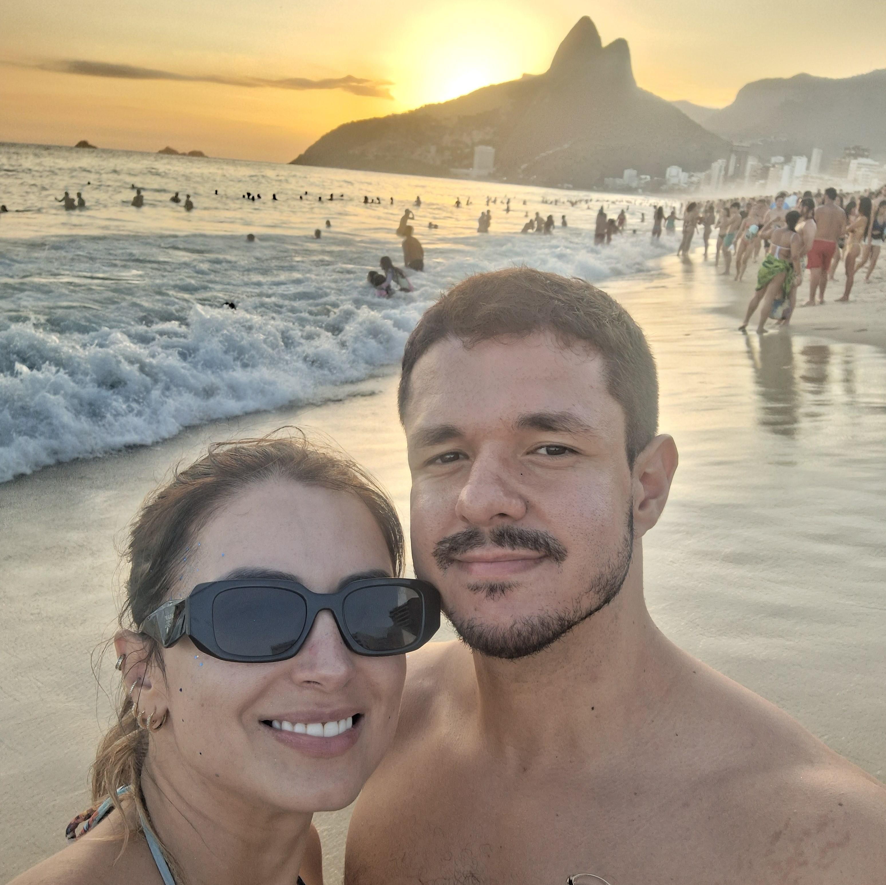 Casal sorrindo junto na praia ao pôr do sol.